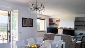 Un coin repas agrémenté d’un lustre, d’une table avec des chaises, d’un canapé et d’un téléviseur en arrière-plan.