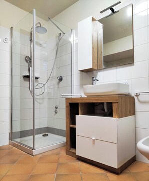 Un baño moderno con ducha envuelta en vidrio, un lavabo blanco, un armario de madera y un espejo sobre el lavabo.
