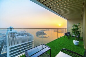 A balcony with a view of a city skyline and water body at sunset. - Palm & Sea View 1BR with Private Beach + Baby Gear (Dubai)