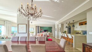 A spacious living room with a large wooden dining table, comfortable seating, a chandelier, and a kitchen area in the background. - Villa Disdant , Fresnaye , Cape Town (Cape Town)