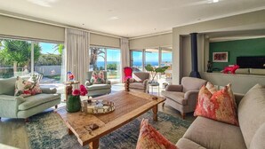 A spacious living room with a large coffee table, sofas, and a view of the ocean. - Villa Disdant , Fresnaye , Cape Town (Cape Town)