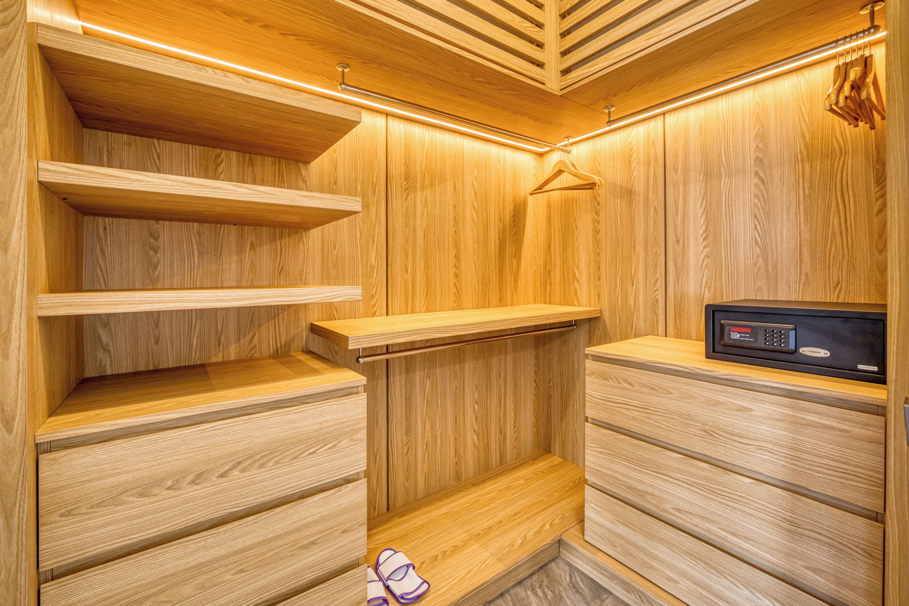 Ein begehbarer Kleiderschrank aus Holz mit Regalen, einer Kleiderstange und einer Bedienkonsole.