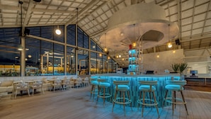 Eine Bar mit Holzboden, Barhocker und einer hohen Decke mit großen Fenstern.