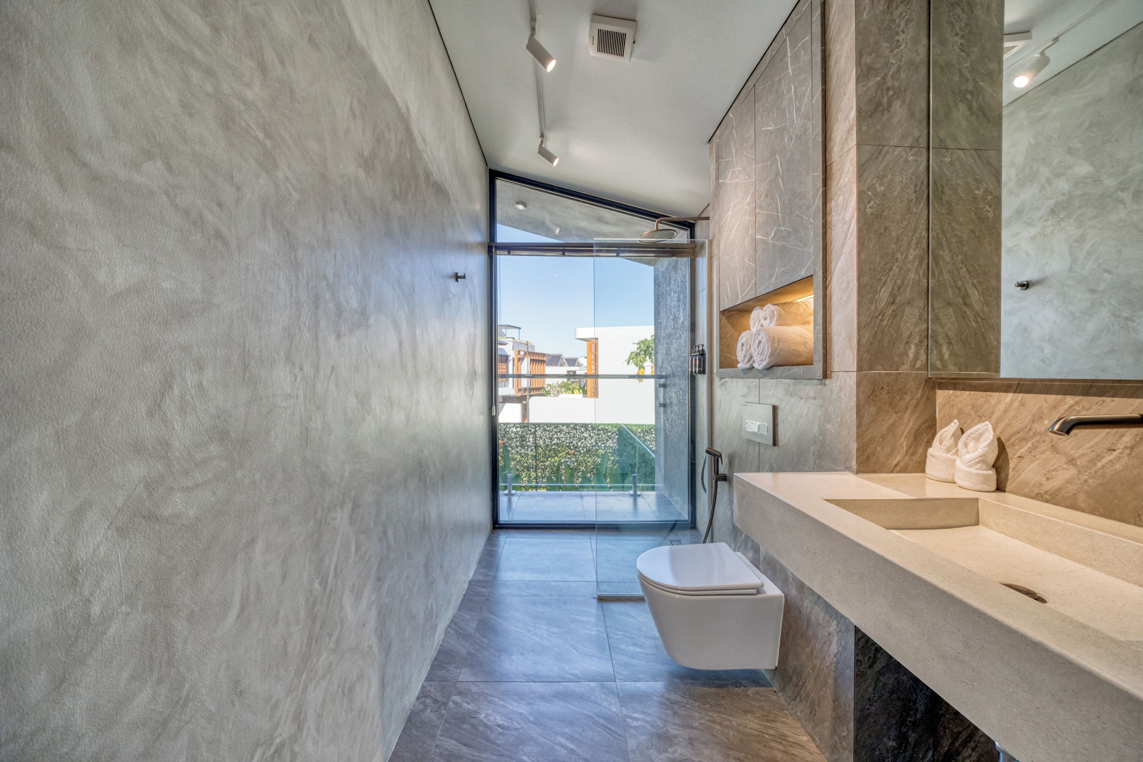 A modern bathroom with a large window, a toilet, a sink, and a shower area.