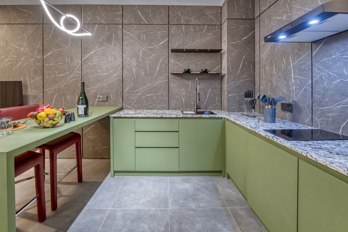 A modern kitchen with a green countertop, a marble backsplash, and a built-in oven.