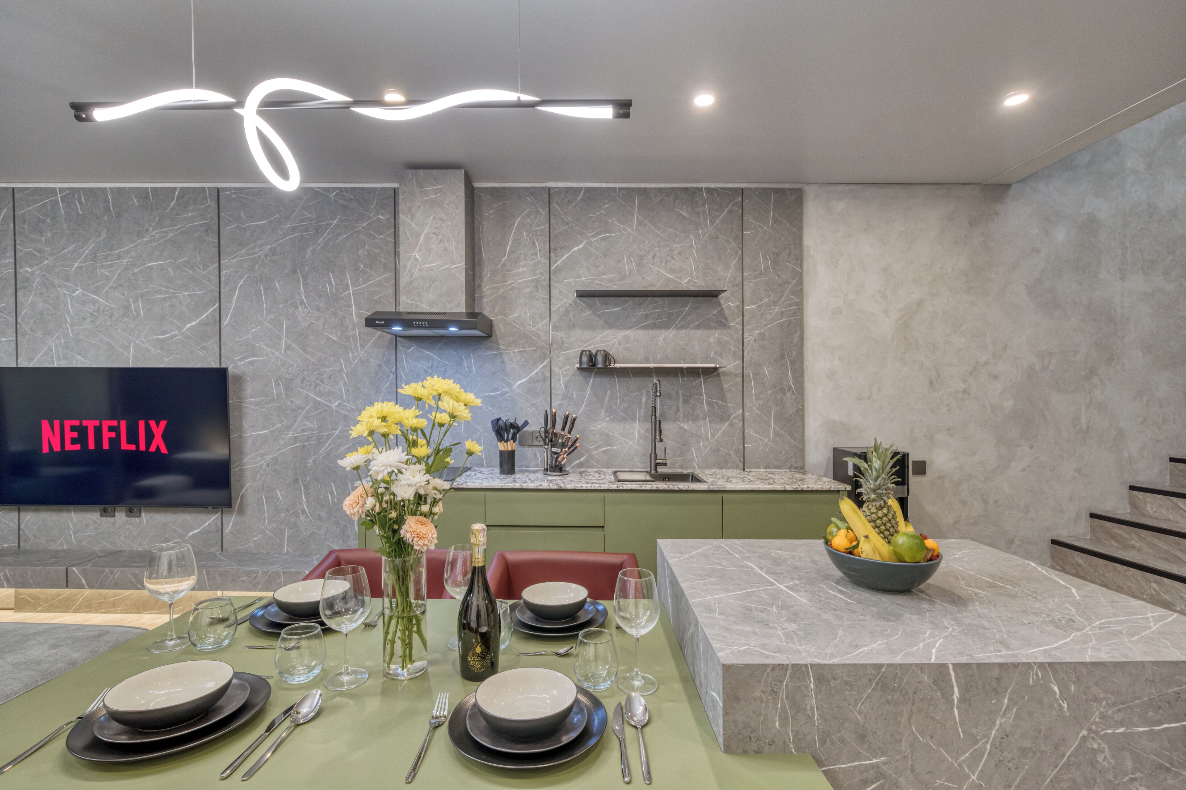 A modern kitchen with a flat-screen TV, marble countertops, and a dining area set for four.