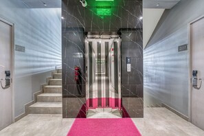 A modern elevator with a digital display, marble walls, and a pink carpet leading to a staircase. - XO Canggu Adults Only (Canggu)