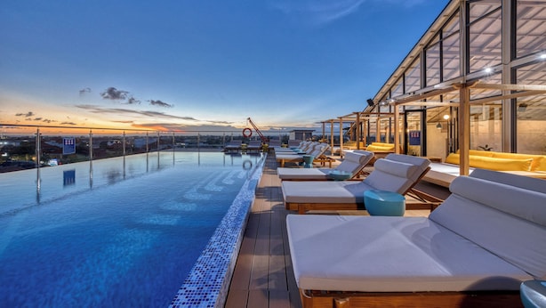 Ein Infinity-Pool auf dem Dach mit Liegestühlen und einer gläsernen Struktur.