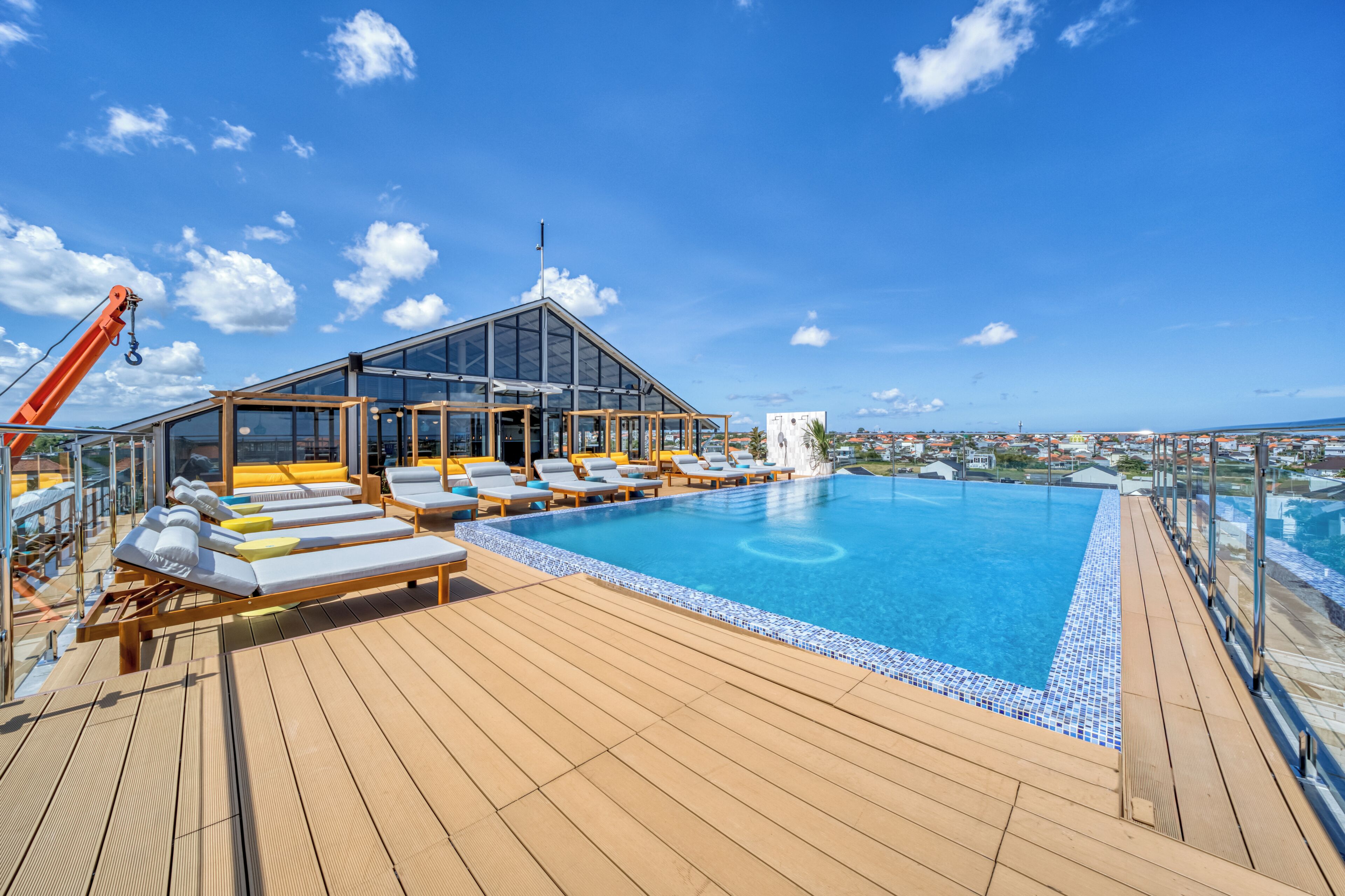 A poolside area with sun loungers, a glass-enclosed structure, and a clear view of the ocean.