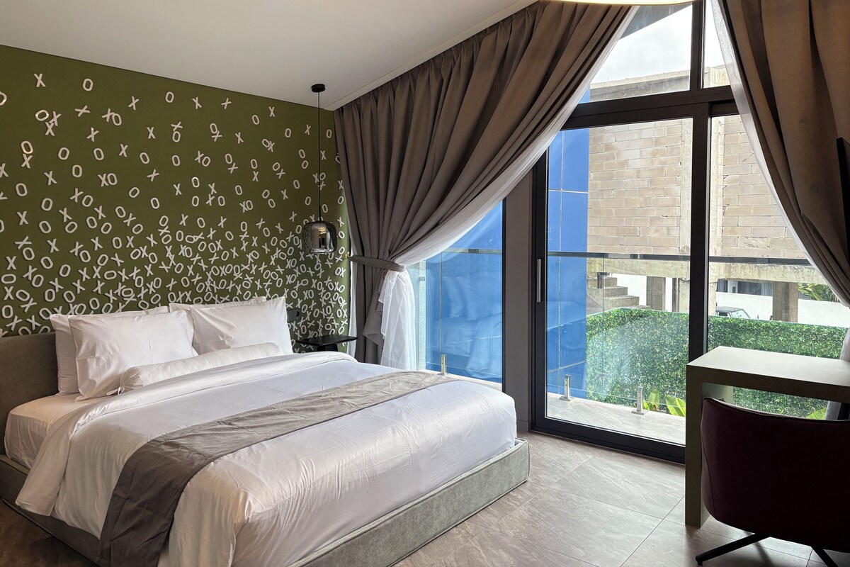 Une chambre d’hôtel avec un grand lit, un bureau, une vue sur l’extérieur et un mur orné d’un motif de lettres.