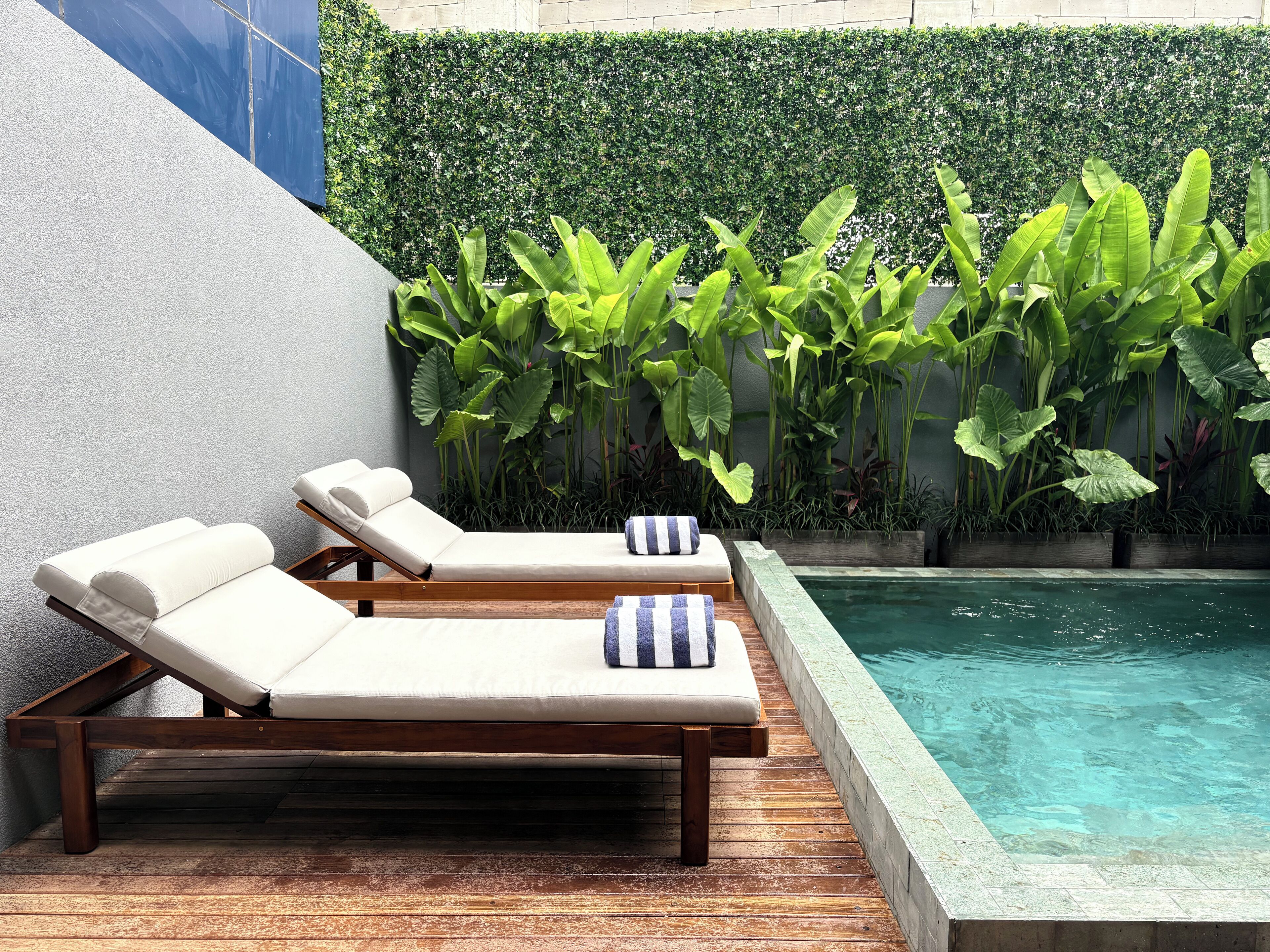 Área da piscina com duas espreguiçadeiras e um deck de madeira.