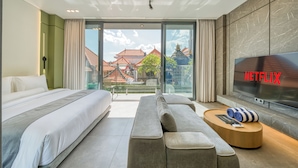 Ein modernes Hotelzimmer mit einem großen Bett, einer Sitzecke, einem Fernseher und einem Balkon mit Blick auf Gebäude.