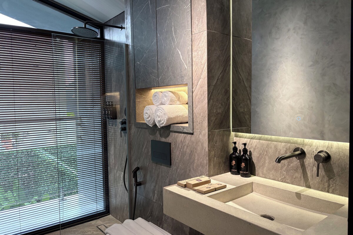 A modern bathroom with a large mirror, a sink with soap dispensers, and a towel rack with neatly rolled towels.