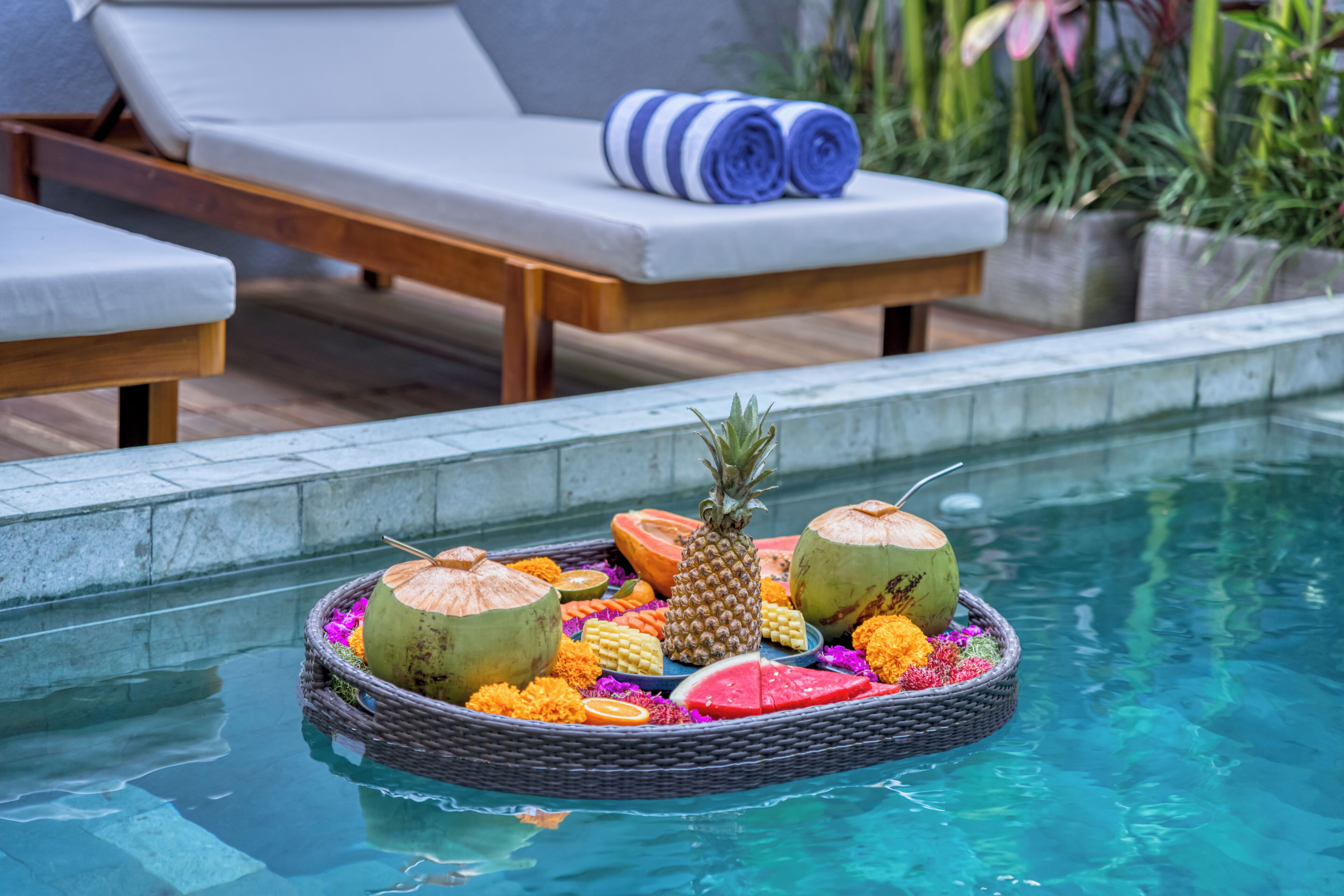 A poolside area with lounge chairs and a floating fruit and flower arrangement.