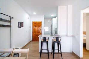 Una cocina moderna con encimera blanca, dos taburetes de bar y una puerta de madera al fondo.