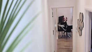 Een gang die uitkomt in een eetgedeelte met een tafel, stoelen, een potplant en een telefoon aan de muur.