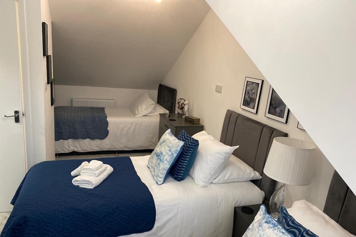 Une chambre d’hôtel avec deux lits, une table de chevet, une lampe et un tableau encadré au mur.