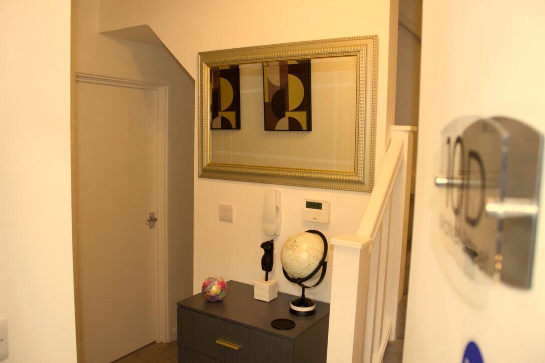 Un couloir avec une porte, une petite table sur laquelle se trouvent un globe terrestre et un téléphone, et une œuvre d’art abstraite encadrée accrochée au mur.