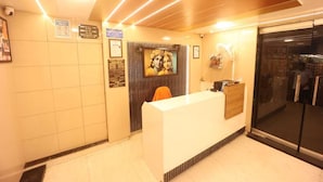 Un espace d’accueil avec un comptoir de réception blanc, un tableau encadré au mur et une porte vitrée donnant sur l’extérieur.