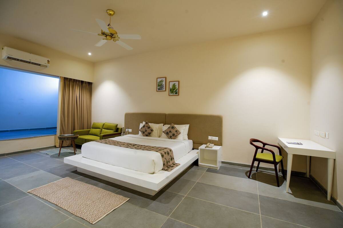 A bedroom with a bed, a desk, a chair, a ceiling fan, and a window with curtains.