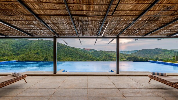 A poolside area with a view of a mountain landscape. - Nanda Hill Resort-Aravali Views (Udaipur)