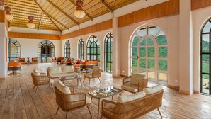 A spacious lounge area with wicker furniture, large arched windows, and a bamboo ceiling. - Nanda Hill Resort-Aravali Views (Udaipur)