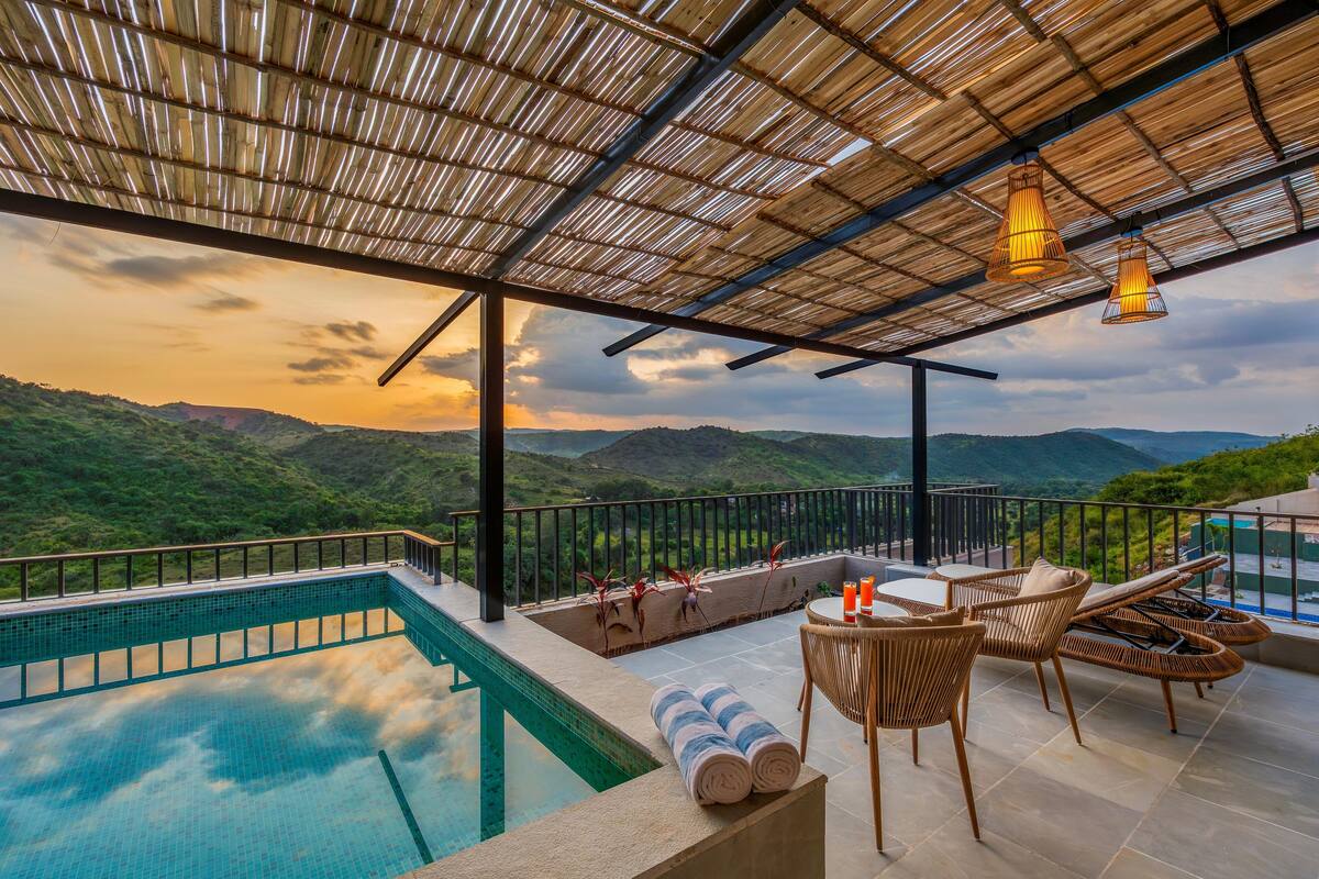 A rooftop pool area with a view of green hills, a pool, and lounge chairs.