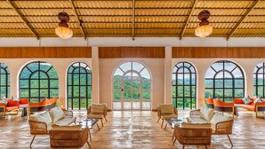 A spacious room with large arched windows, wooden flooring, and wicker furniture. - Nanda Hill Resort-Aravali Views (Udaipur)