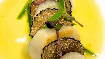 A dish with sliced fish, greens, and a yellow sauce on a white plate.