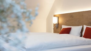 A neatly made bed with white linens and two red pillows in a room with a wooden headboard and a wall-mounted light fixture. - Landhotel Steigenhaus (Untermünkheim)