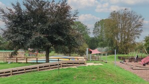 A playground with a swing set, a slide, and a sandbox area surrounded by a wooden fence. - Molly (Woodbridge)