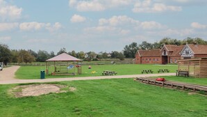 Ein Park mit Picknicktischen, einem Spielplatz und einem traditionellen Gebäude mit rotem Dach.