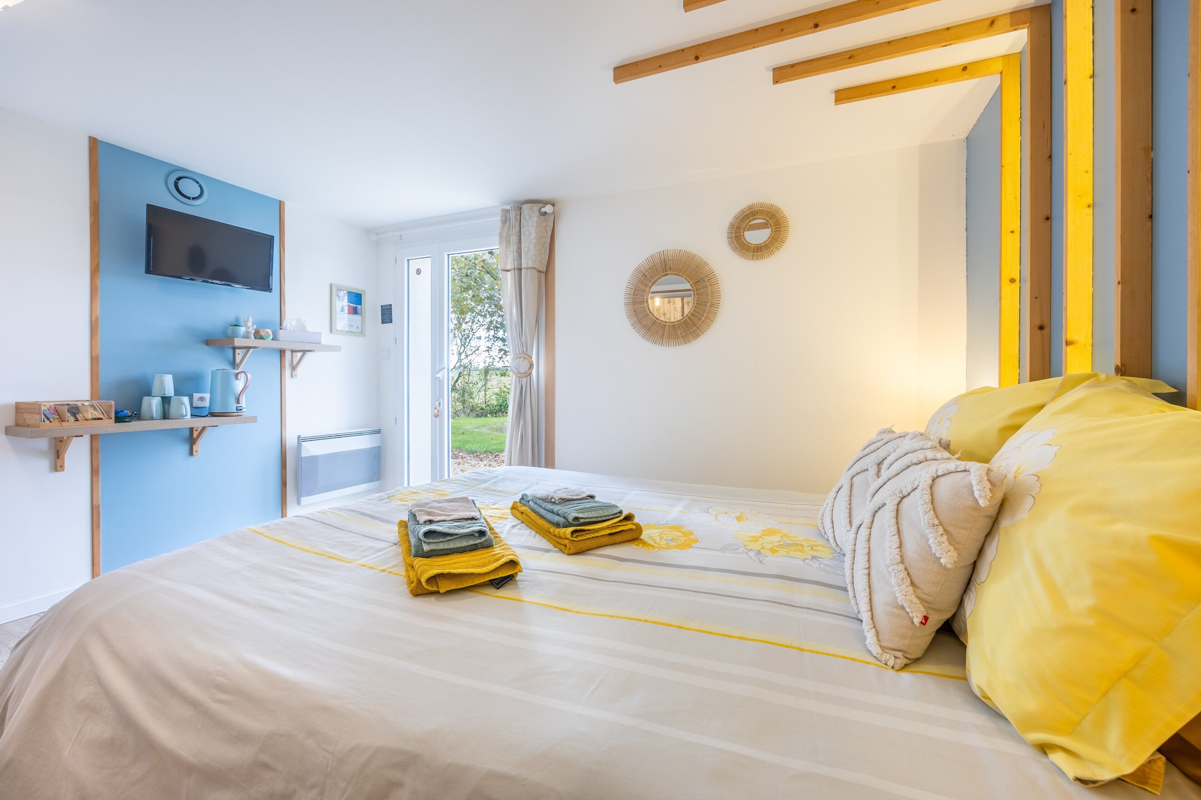 Un dormitorio con cama, televisor montado en la pared, puerta que da a un balcón y ventana con cortinas.