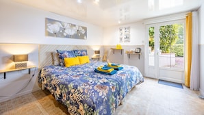 Un dormitorio con cama, mesitas de noche, una lámpara de pared, una puerta que da a un balcón y una ventana con cortinas.