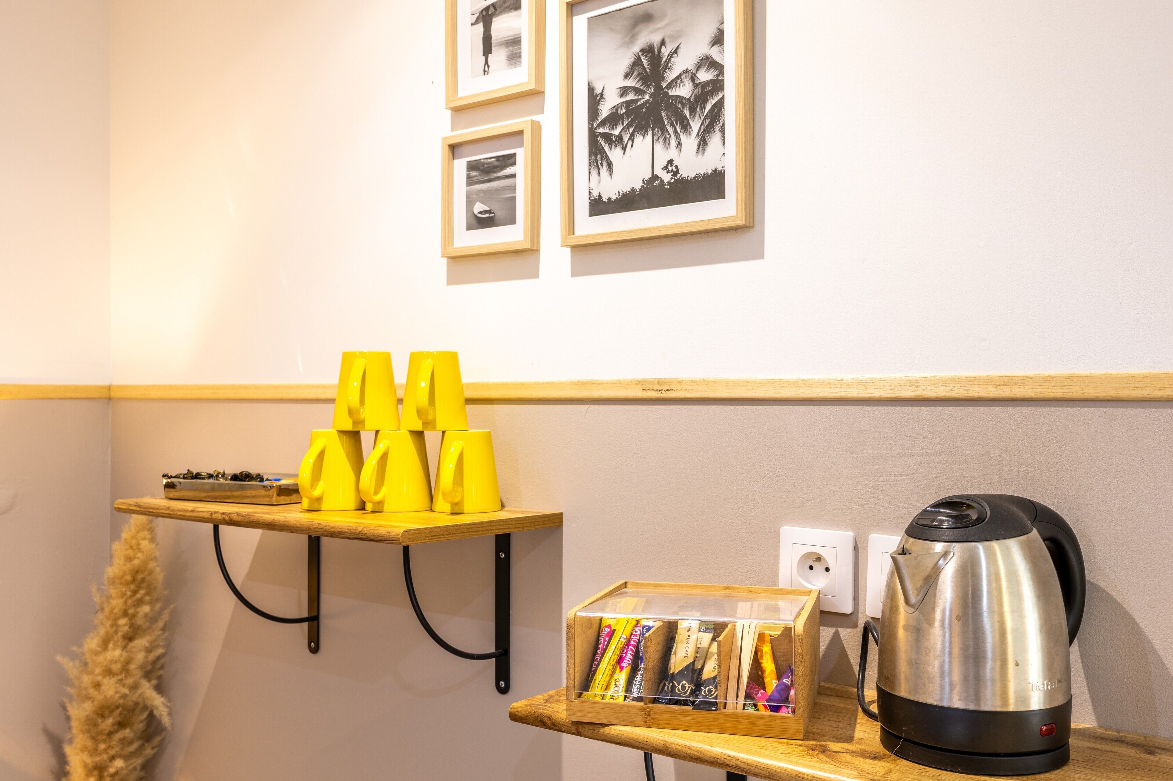 A kitchen area with a coffee machine, a shelf with yellow cups, and a box of tea bags.