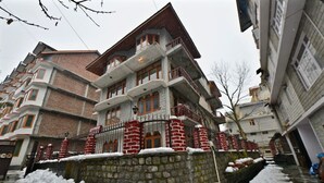 A multi-story building with a stone base and brick upper levels, featuring balconies and a central entrance. - Hotel Potala Manali (Manali)