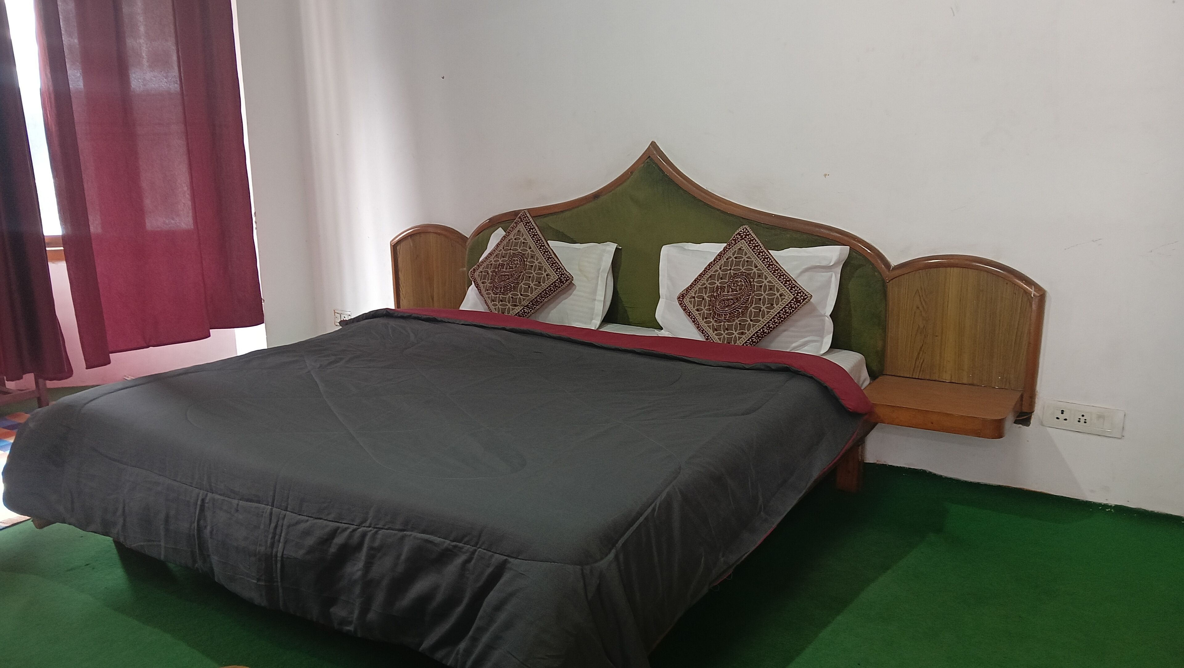 Una cama con cabecera verde, dos almohadones decorativos y una colcha roja.