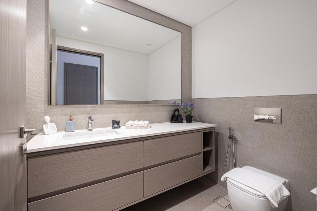 A modern bathroom with a large mirror, a white sink, and a toilet.