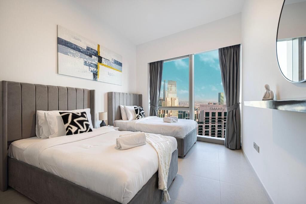 Ein modernes Hotelzimmer mit zwei Betten, einem großen Fenster mit Vorhängen, Blick auf die Stadt und einem aufgehängten Kunstwerk.