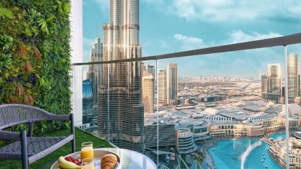 A balcony with a glass table set with breakfast, overlooking a cityscape with a prominent skyscraper.