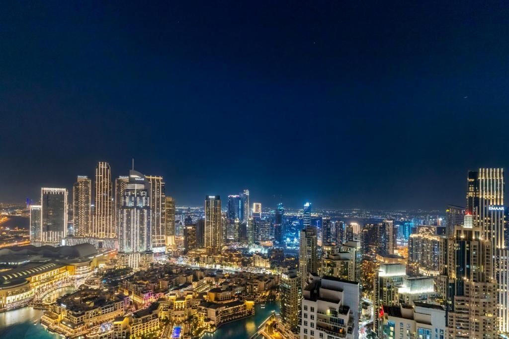 Un paisaje urbano nocturno con edificios altos iluminados y una zona ribereña.