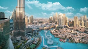 A cityscape with modern high-rise buildings, a central water feature, and a clear sky.