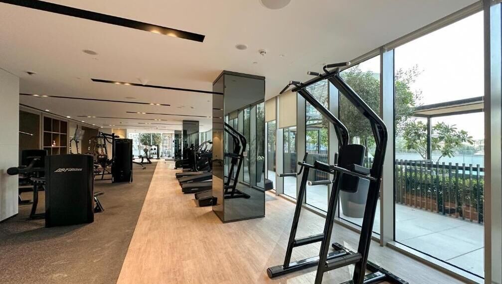 Ein modernes Fitnessstudio mit Cardiogeräten, Krafttrainingsgeräten und einem großen Fenster mit Blick ins Freie.