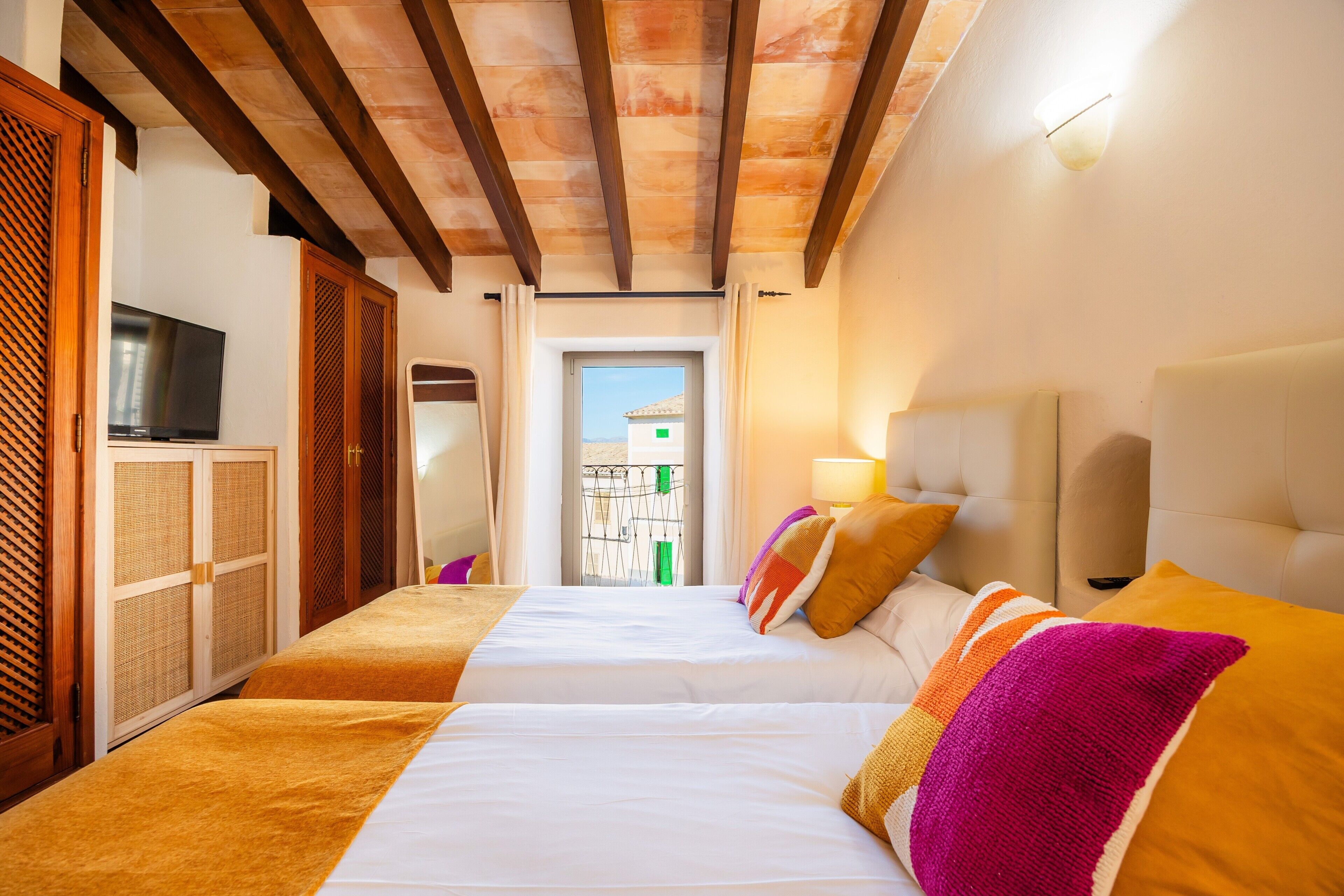 A hotel room with two beds, wooden beams on the ceiling, a TV, and a view through a door.