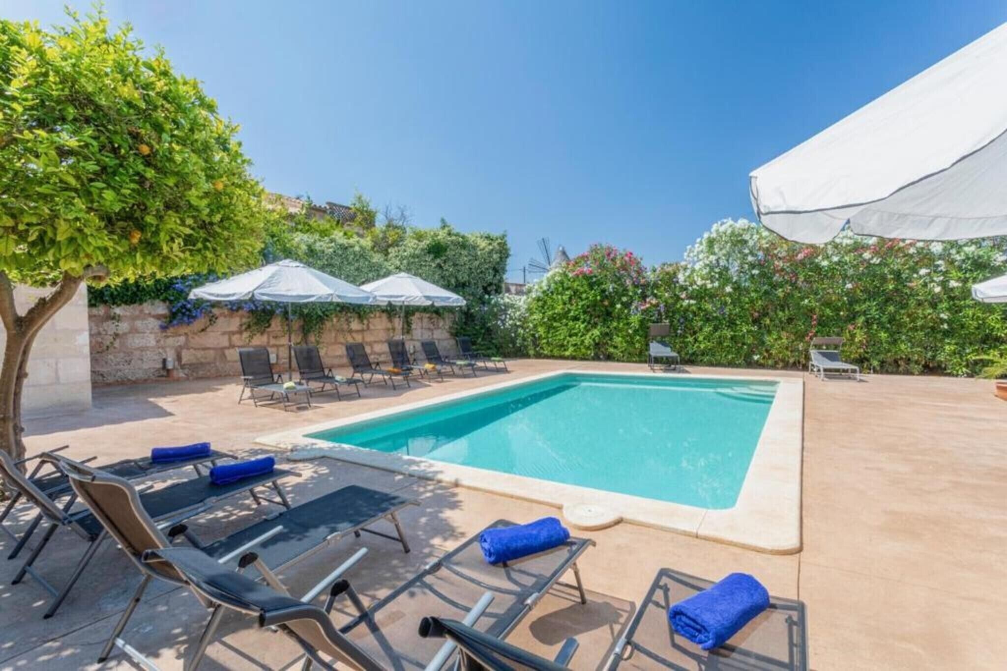 Une piscine rectangulaire entourée de verdure et d’un mur de pierre, avec des chaises longues et des parasols.