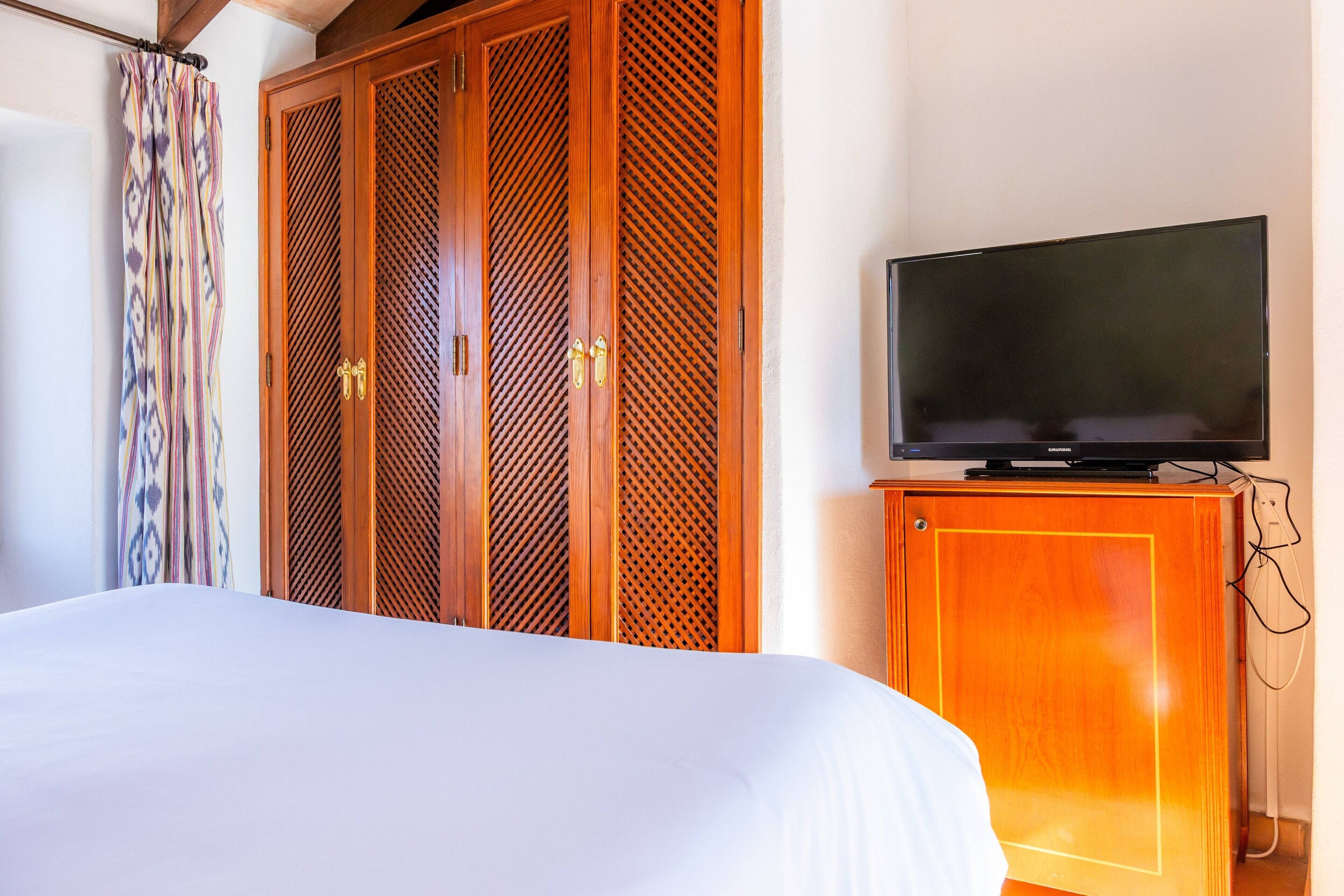 Ein Hotelzimmer mit einem Bett, einem Fernseher auf einer Holzkommode und einem gemusterten Vorhang.
