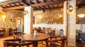 Un coin repas rustique avec des tables et des chaises en bois, des murs en pierre et des assiettes décoratives.