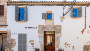Un bâtiment sur lequel on peut lire l’inscription « SA BARCELLA », avec une porte en bois et deux plantes en pot.