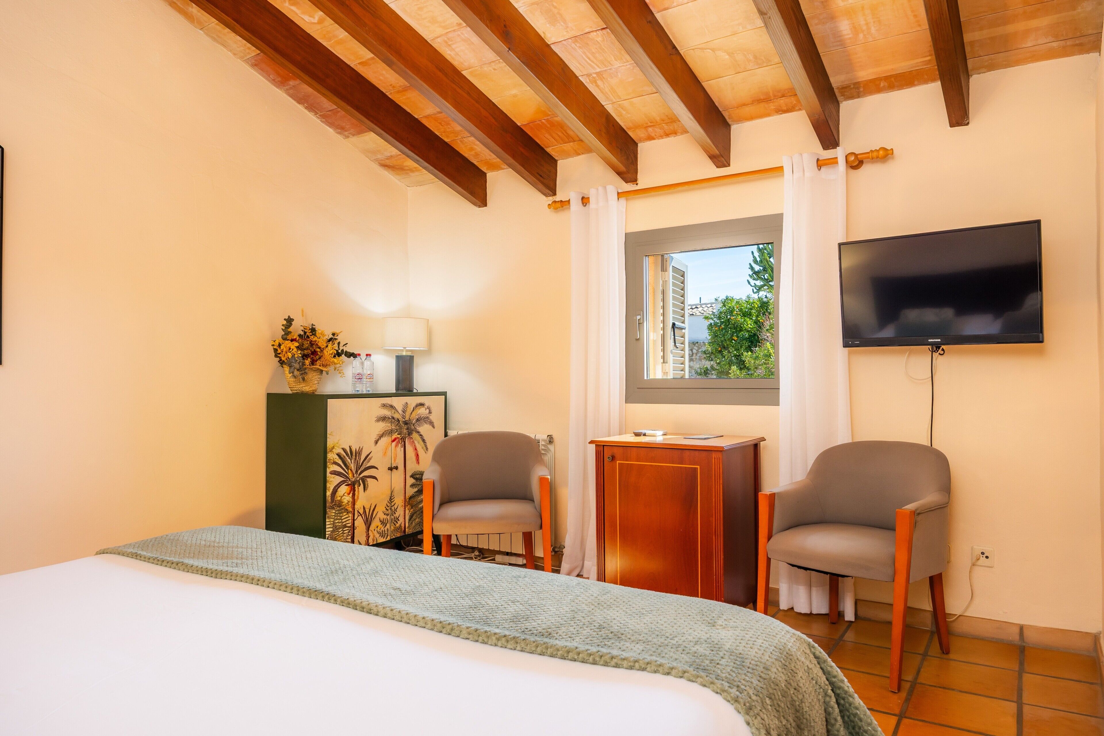 A hotel room with a bed, two chairs, a desk, a TV, and a window with a view.