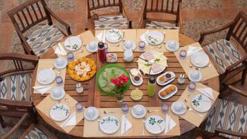 Een ronde houten tafel met stoelen, gedekt voor een maaltijd met borden, bestek en diverse soorten eten.